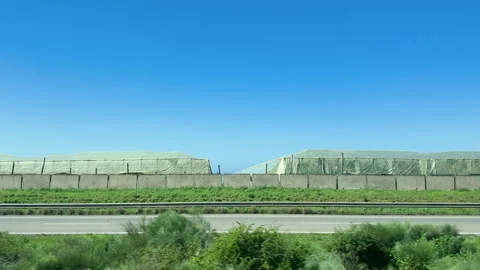 Traveling view from a moving car window showing large greenhouses alongside Stock Footage 339436220