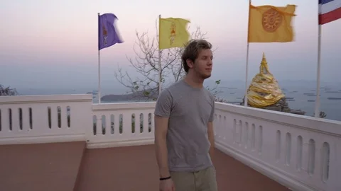 Traveller Hitting Large Bell at Temple and Looking at View of Island From Hill Stock Footage 126575828
