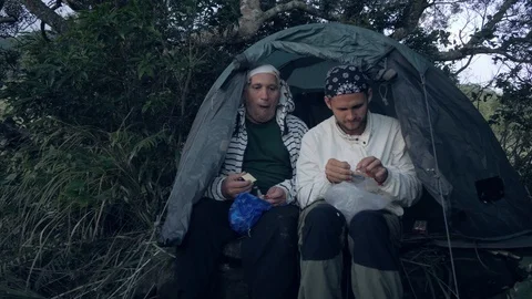Travellers men having dinner sitting in tent in forest camping in evening. Stock Footage 118412364