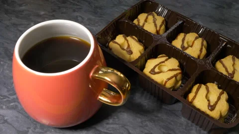 A tray of biscuits being pushed next to a cup of steaming black coffee. Stock Footage 154396352