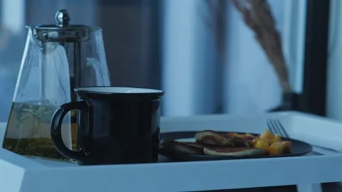 Tray with breakfast staying on the bed. Pancakes with fruits and hot tea, hotel Stock Footage 254486014