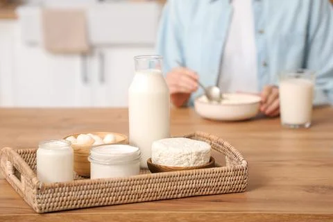 Tray with different dairy products on table against woman in kitchen, closeup Stock Photos