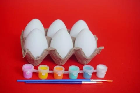 Tray or box of six eggs on red background, multi-colored paints and brushes.  Foto stock