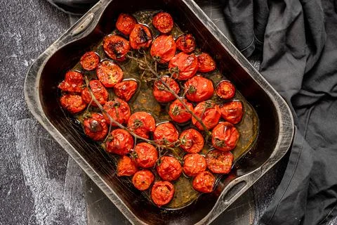 Tray of roasted red cherry tomatoes with garlic, herbs and olive Stock Photos
