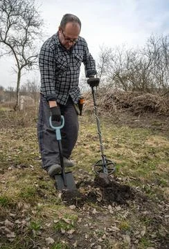 A treasure hunter stands in a field using a metal detector while digging in.. Stock Photos