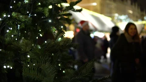 A tree branch decorated with Christmas lights, people walk at a Christmas market Stock Footage 132875261