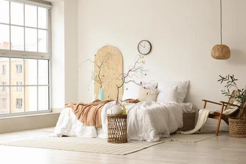 Tree branches decorated with Easter eggs on tables and comfortable bed in bed Stock Photos