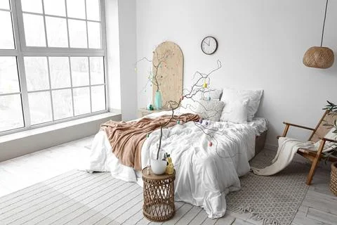 Tree branches decorated with Easter eggs on tables and comfortable bed in bed Stock Photos