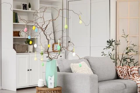 Tree branches decorated with Easter eggs on stylish table and comfortable gre Stock Photos