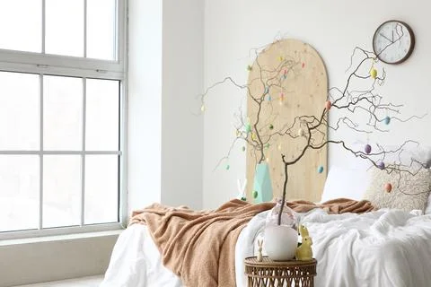 Tree branches decorated with Easter eggs on tables and comfortable bed in bed Stock Photos