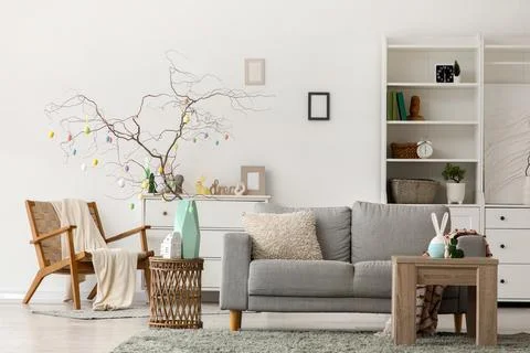 Tree branches decorated with Easter eggs on stylish table and comfortable gre Stock Photos