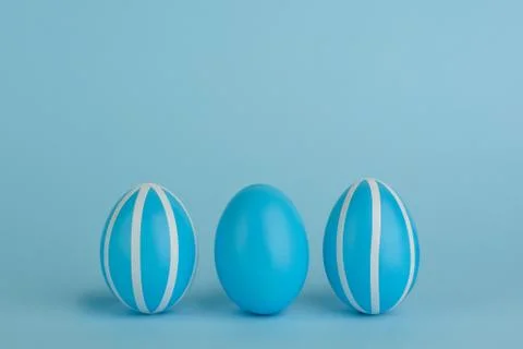 Tree Easter decorated blue eggs in a row. Blue background. Copy space. Stock Photos
