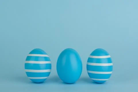 Tree Easter decorated blue eggs in a row. Blue background. Copy space. Stock Photos