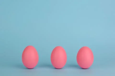 Tree Easter decorated pink eggs in a row. Blue background. Copy space. Stock Photos