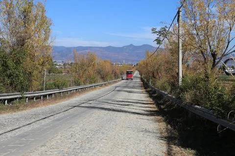 Tree-lined cobblestone road with a small red vehicle in the distance Foto stock