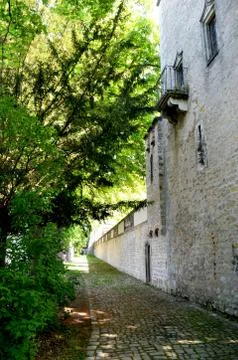 A tree-lined path beside a stone wall of a house. Stock Photos