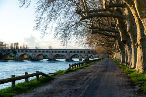Tree Lined River Road Leading Toward Stone Bridge Stock Photos