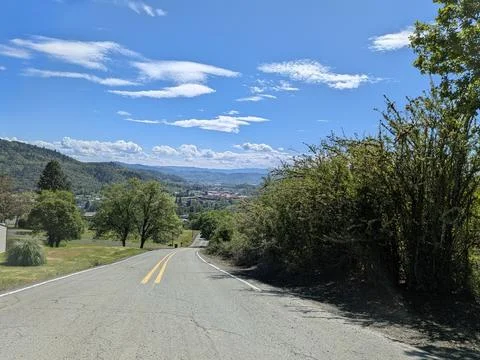 Tree-lined road leading toward a peaceful town beneath forested hills Foto stock