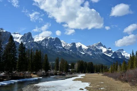 Tree-lined stream with snow and mountain range Stock Photos