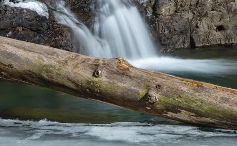 Tree Log Laying on Iced River with Waterfall Stock Photos