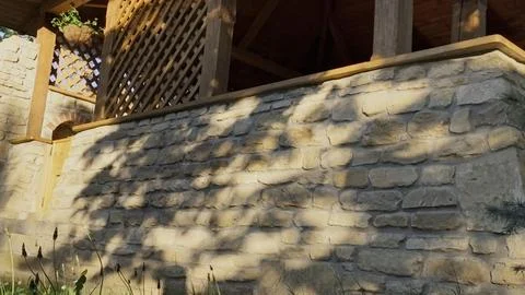Tree shadows dancing on a rustic stone wall and a wooden terrace Stock-Fotos