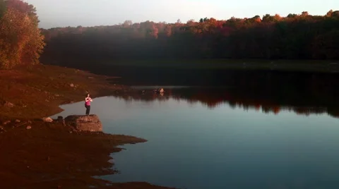 Tree to upward salute yoga poses on rock near lake Stock Footage 44118908