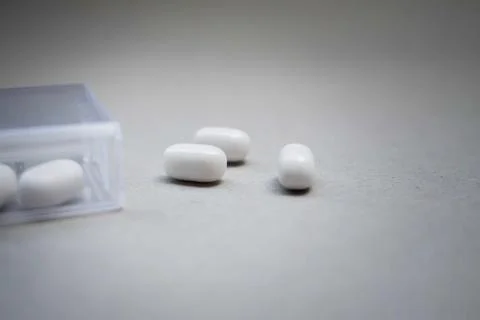Tree white capsules on a white background and a transparent container near it Stock Photos