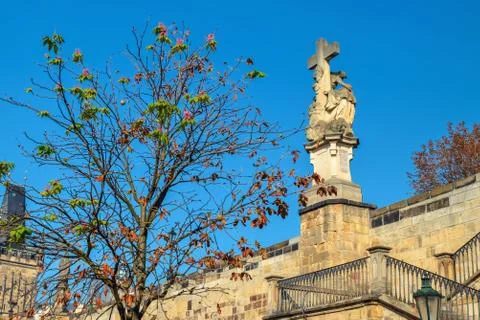 Tree without leaves and a statue with a cross in Prague in autumn Stock Photos