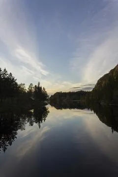 Trees and blue sky reflected on calm blue water Stock Photos