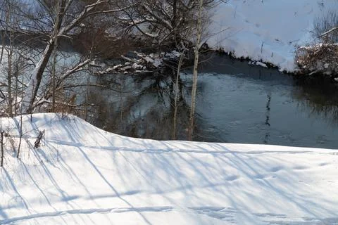 Trees covered with snow and footprints in the snow along the bank of a small  Stock Photos
