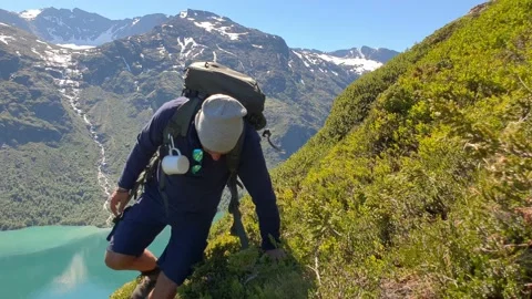Trekker sits down at a mountainside infront of turqouise lake in Norway Stock Footage 156786398