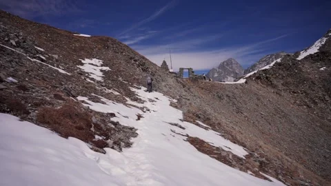 Trekker walking uphill along a snow dusted mountain trail toward a small stone Vídeos de archivo 344181932