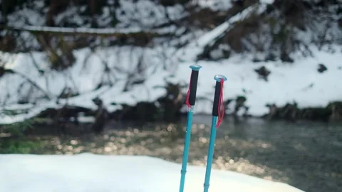 Trekking poles stand stuck in the snow near the mountain river Stock Footage 241908783