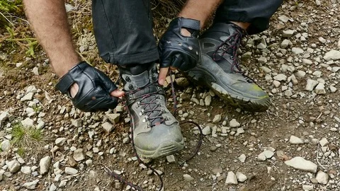 Trekking through the mountains. A man ties up his shoelaces on trekking shoes 動画素材 77169981