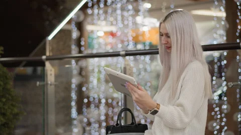 Trendsetter tapping smartphone on mall bench under festive lights Stock Footage 316825324