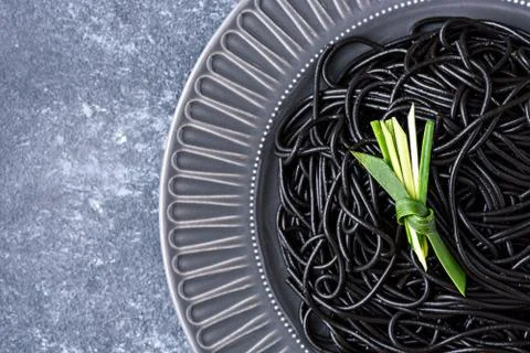 Trendy black paste with cuttlefish ink in grey plate with leaf on grey backgr Stock Photos