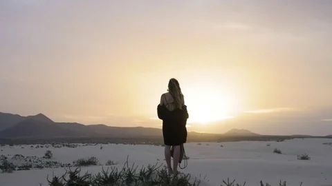 Trendy blonde woman standing on sand dune during sunset Stock Footage