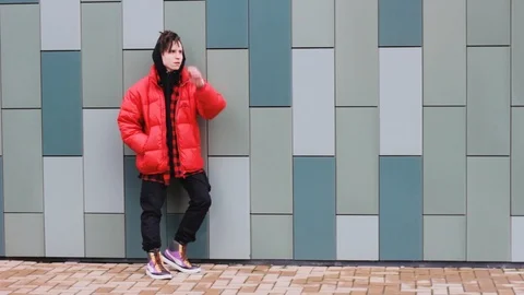 Trendy guy standing at the wall in a red jacket and looking to the camera 스톡 동영상 123863798