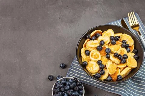 Trendy home breakfast with tiny pancakes and blueberry on gray concrete backg Stock Photos