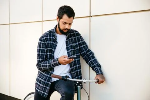 Trendy man using a smartphone while sitting on bike, outside Stock Photos