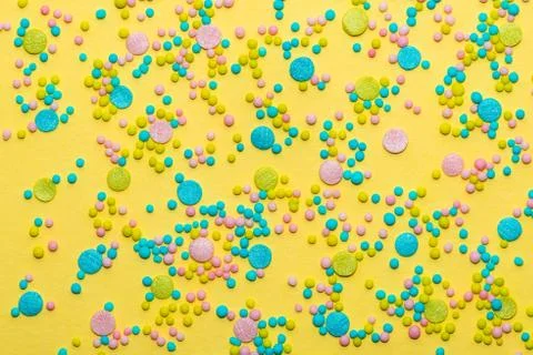 Trendy pattern of colorful round sprinkles over yellow background, decoration Stock Photos