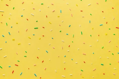 Trendy pattern of colorful sprinkles over yellow background, decoration for c Stock Photos