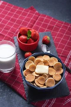 Trendy tiny cereal pancakes with slice of butter in blue bowl, strawberries,  Stock Photos