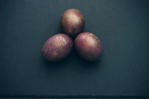 Triangle of 3 magical space cosmic purple marble eggs on black slate board. Stock Photos