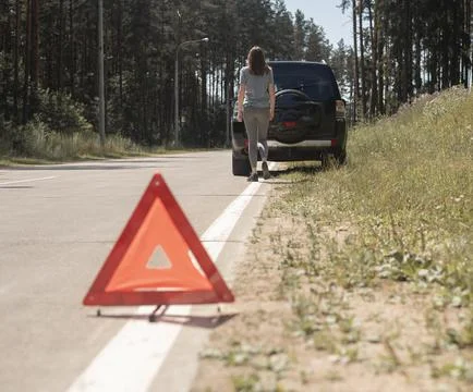 Triangle caution sign closeup on road with young woman going to car on backgr Stock Photos