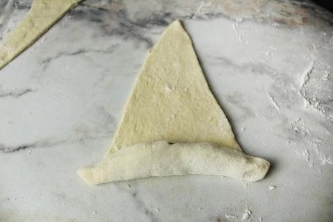 A triangle of raw puff pastry is wrapped in a croissant. Making croissants Stock Photos