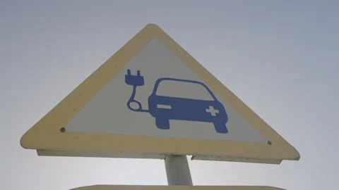Triangle road sign with ev symbol and plug icon mounted on pole at urban street Stock Footage 259842273