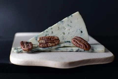 Triangle slice of blue cheese with pecan nuts on wooden board. Stock Photos