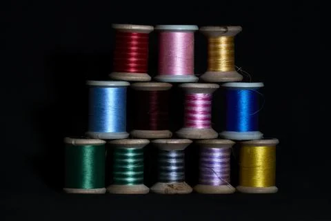 Triangle stack of vibrant sewing machine thread cones on dark background 写真素材