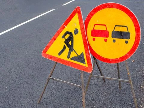 Triangular and circular road signs stand on a freshly asphalted road with drawn Stock Photos